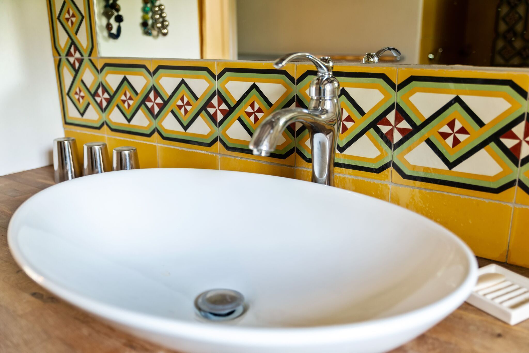 A bathroom with a white sink, a silver faucet, and a yellow and green patterned tile backsplash.