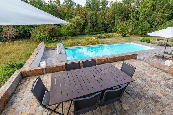 A backyard with a swimming pool, a wooden deck, and a table with chairs.