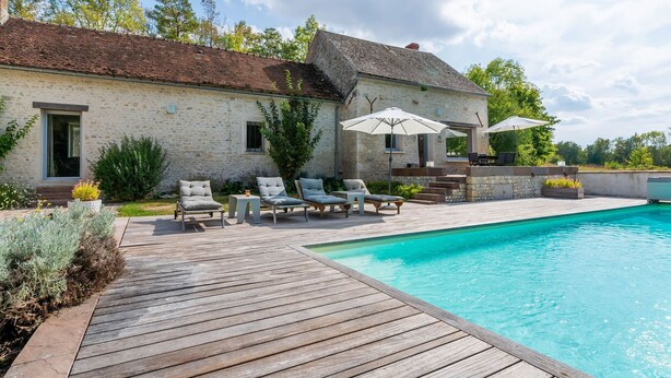A stone house with a wooden deck, a swimming pool, and outdoor seating. - Farmhouse in Yèvre-le-Châtel with Heated Pool (Yèvre-la-Ville)