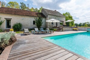 A stone house with a wooden deck, a swimming pool, and outdoor seating.