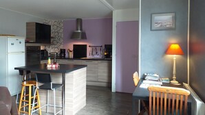 A compact kitchen with modern appliances, a dining area with a table and chairs, and a small island with bar stools. - Modern flat in Bayeux in the town centre (Bayeux)
