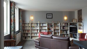 A living room with a brown leather sofa, a dining table, and a bookshelf filled with books. - Modern flat in Bayeux in the town centre (Bayeux)