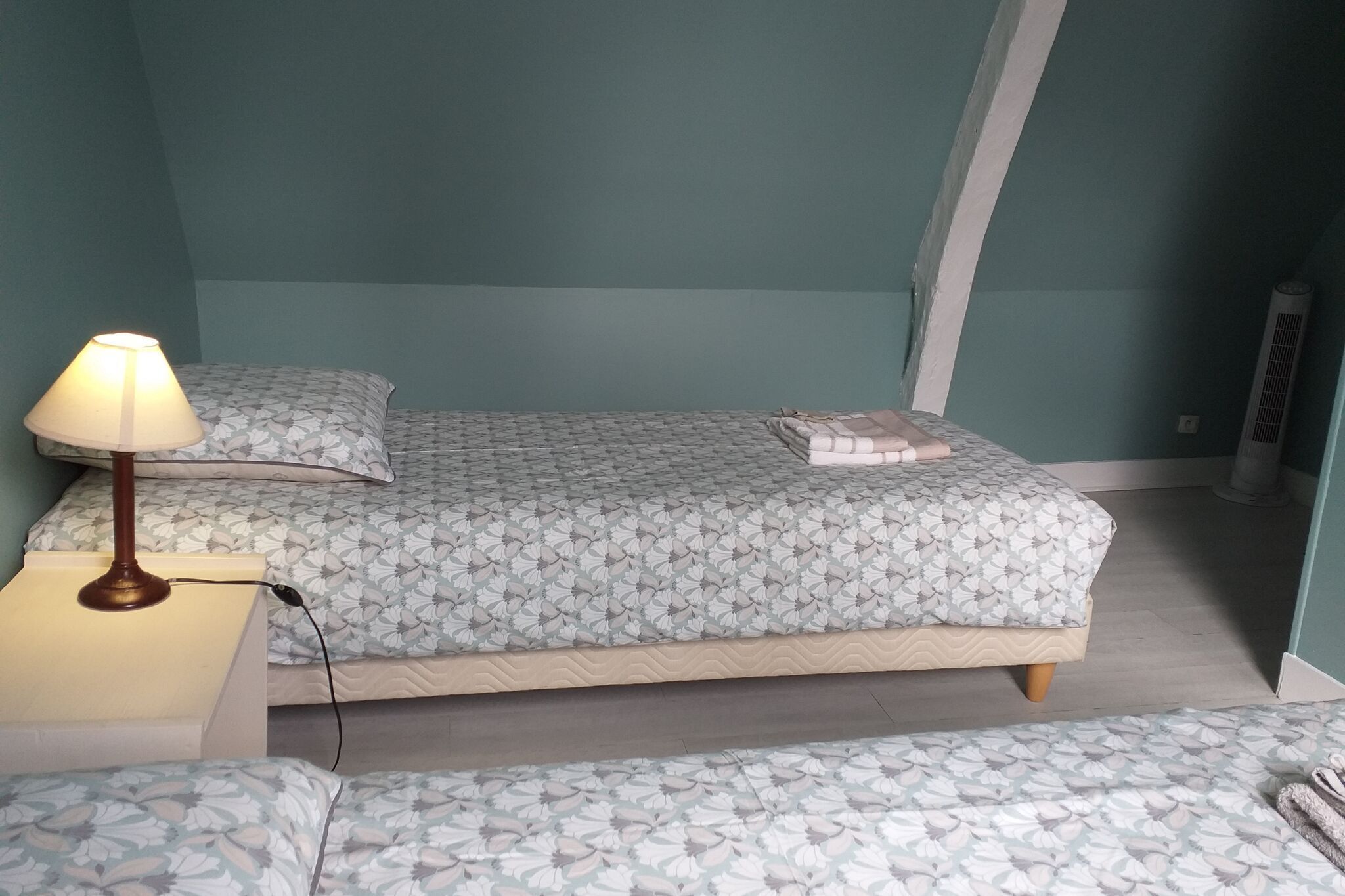 A small, compact room with a bed, a bedside table with a lamp, and a bench.