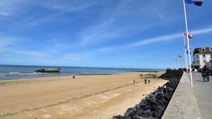 A beach with a row of flags, a rocky breakwater, and a building with a balcony. - Modern flat in Bayeux in the town centre (Bayeux)