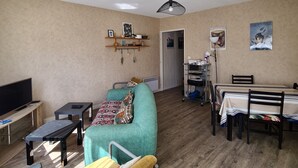 A living room with a sofa, a TV, a dining table with chairs, and a ceiling fan. - Aquarium district, near Old Port, private parking (La Rochelle)