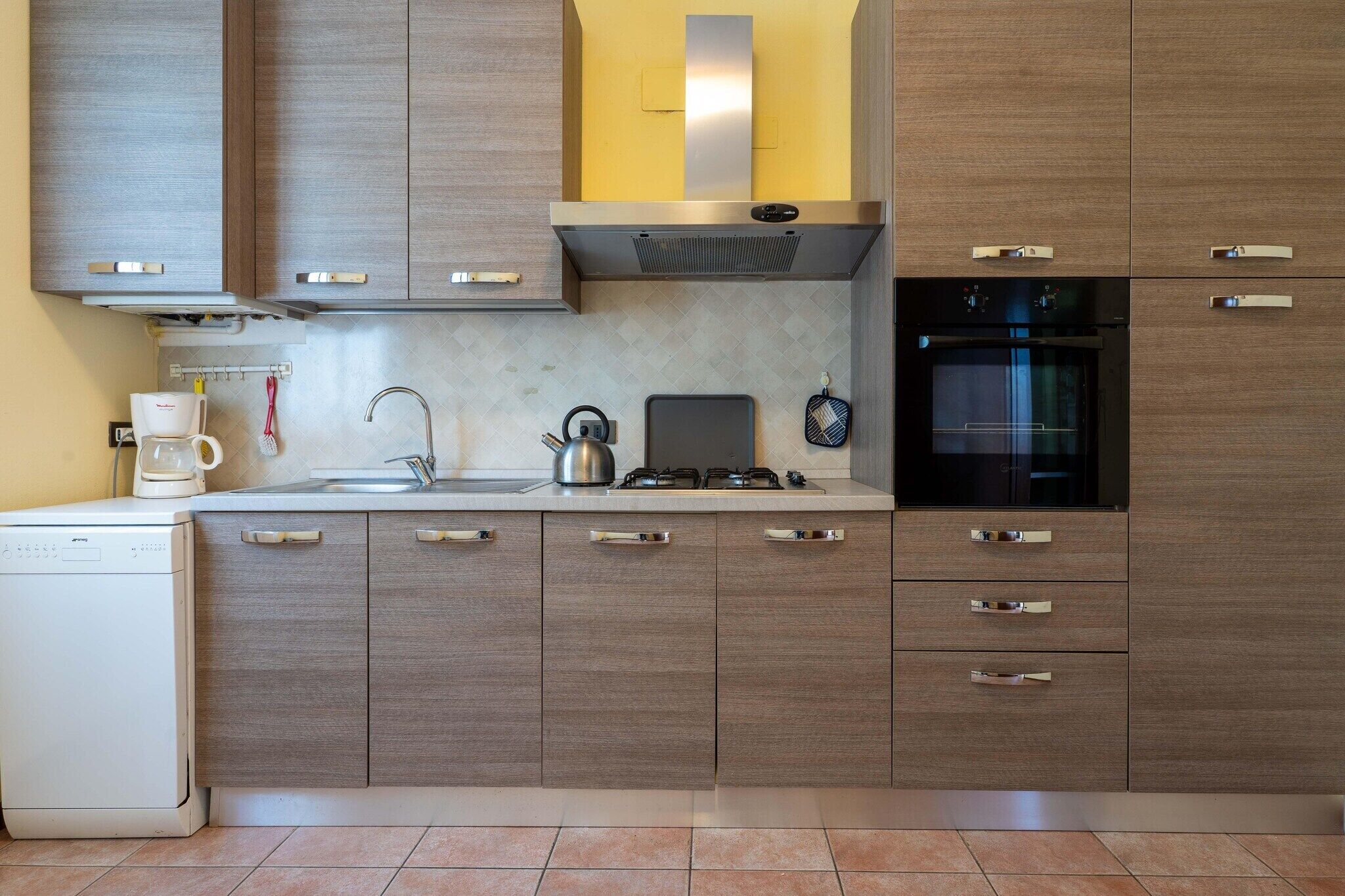 A modern kitchen with wooden cabinets, a built-in oven, a coffee maker, and a kettle.