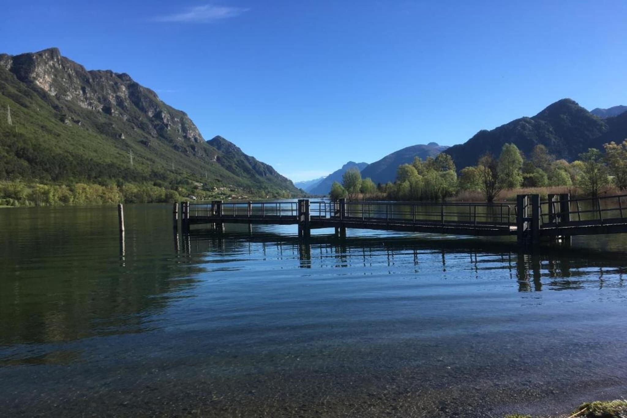 Eine Brücke über einen stillen See, im Hintergrund Berge.