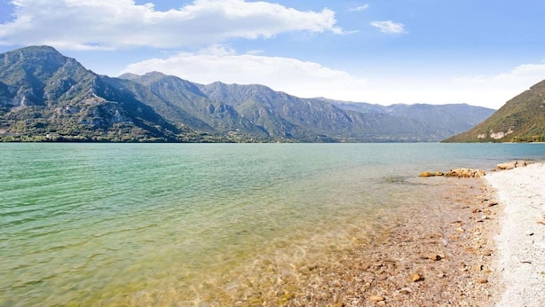 Un lago sereno con una orilla rocosa y montañas al fondo.