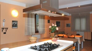 Una cocina moderna con estufa a gas, un ventanal con cortinas y un comedor con mesa y sillas.