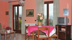 A dining area with a table covered in a pink tablecloth, surrounded by wooden chairs. A potted plant with flowers is on the table. - Holiday Home in Idro near Scenic Hills (Idro (bs))
