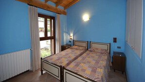A bedroom with two beds, wooden ceiling beams, a window with curtains, a bedside table, and a wall-mounted light. - Holiday Home in Idro near Scenic Hills (Idro (bs))