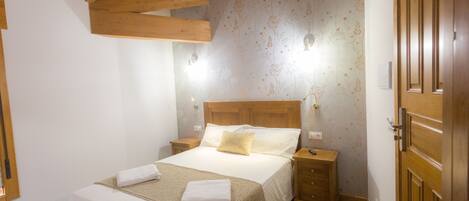 A bedroom with a wooden ceiling, a large bed with a headboard, two bedside tables, and a wooden wardrobe.