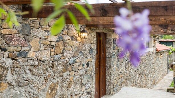 A stone building with a wooden door and a stone wall. - Casa da Ponte de Penas (Melide)