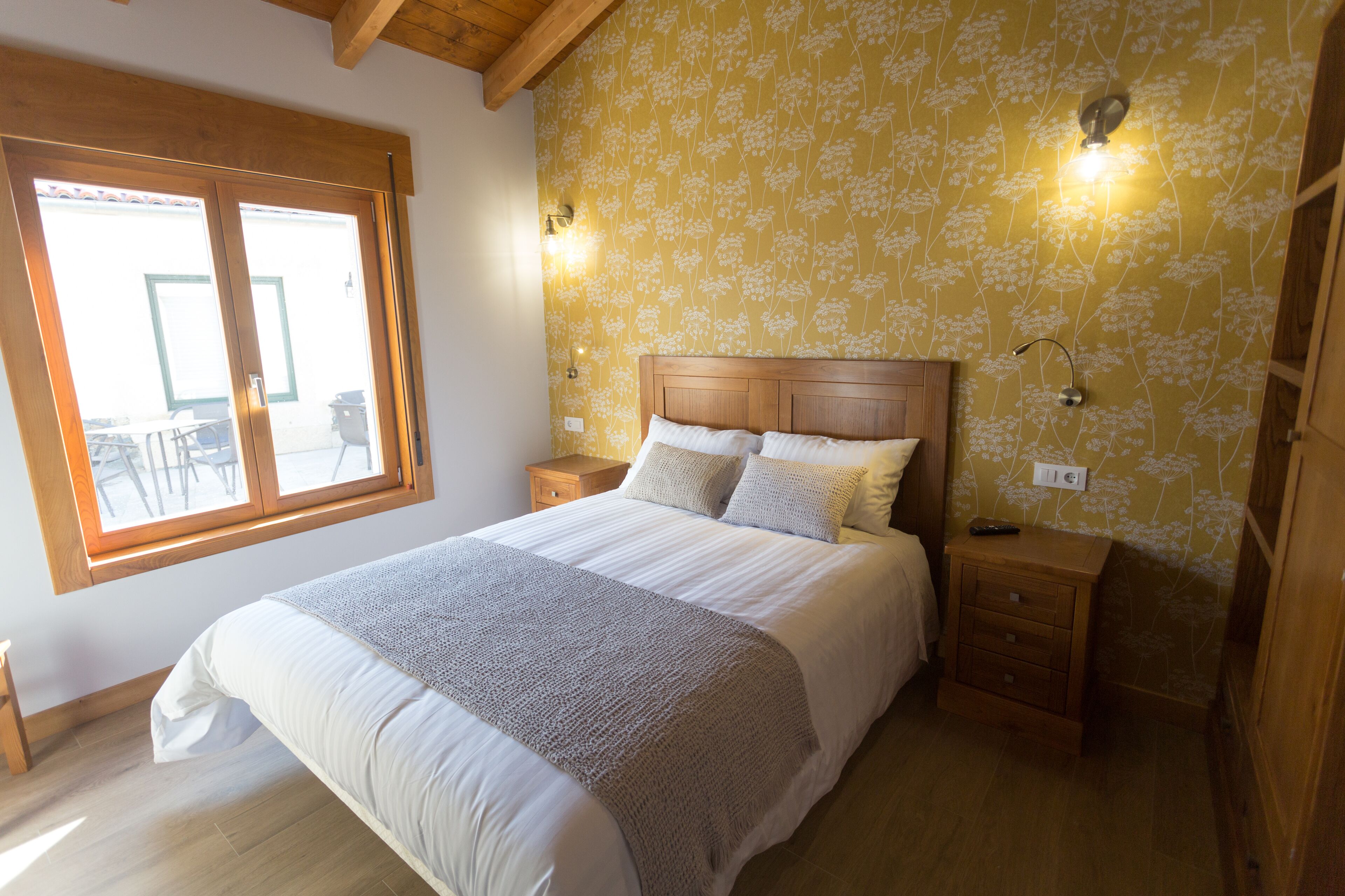 A bedroom with a large bed, wooden headboard, two bedside tables, and a window with a view.