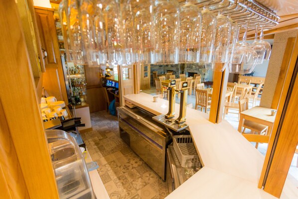 A bar area with a counter, stools, and hanging wine glasses. - Casa da Ponte de Penas (Melide)