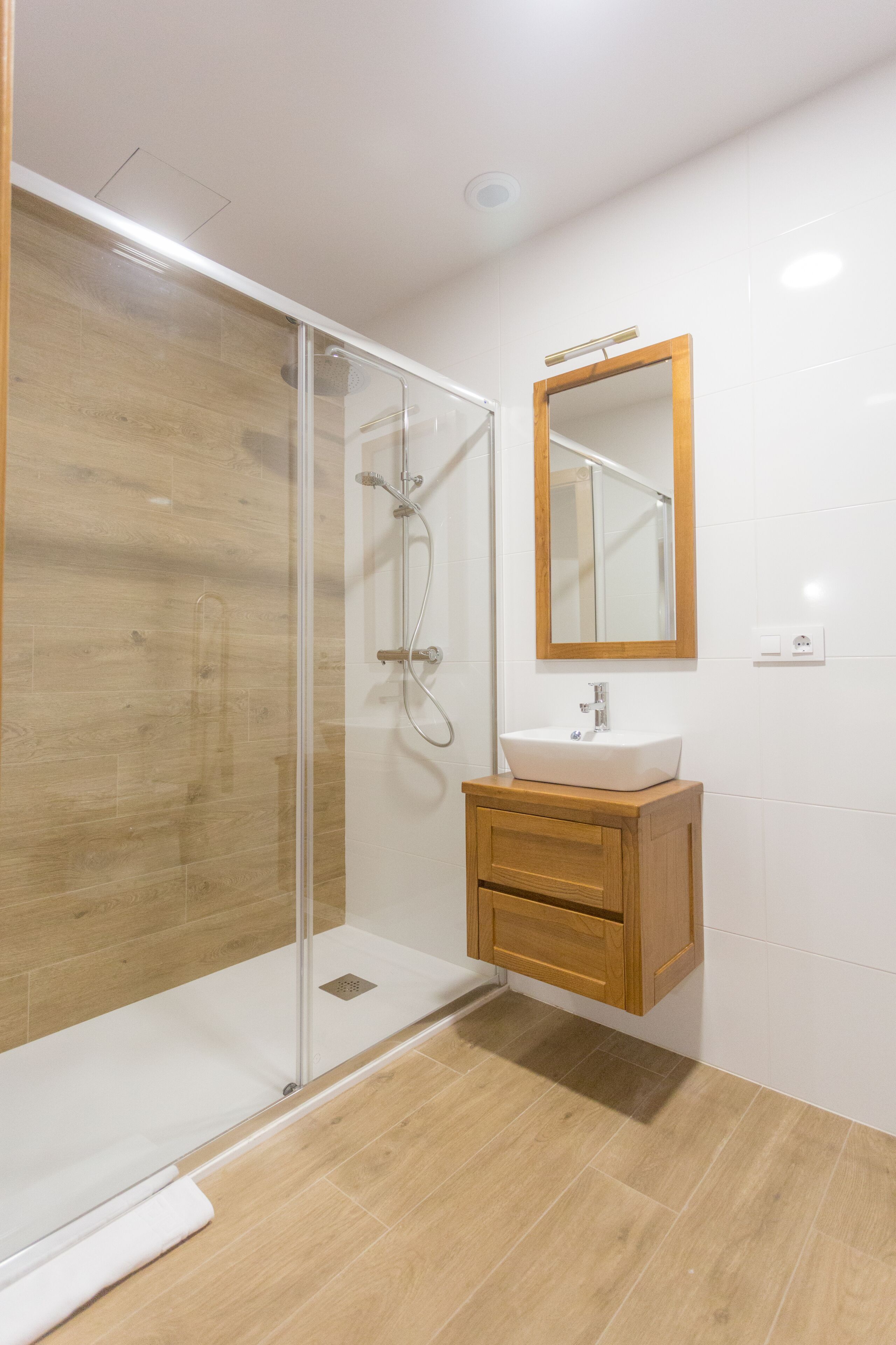 A modern bathroom with a glass shower enclosure, a wooden vanity, and a mirror.