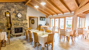 A dining area with stone walls, wooden beams, and tiled flooring. Tables are set with white tablecloths and chairs. - Casa da Ponte de Penas (Melide)