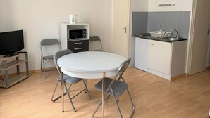 A compact living space with a round dining table, two chairs, a TV, a microwave, a small kitchen area with a sink, and a cabinet. - Studio Centre Ville et Bord de mer (Les Sables-d'Olonne)