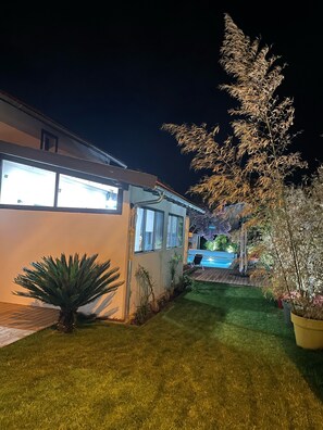 Une maison avec une pelouse bien entretenue, une piscine et un grand arbre.