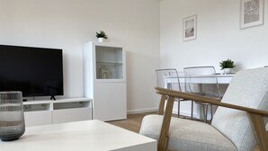 A modern living room with a flat-screen TV, a glass-top coffee table, a white cabinet, a dining area with a table and chairs, and a grey sofa. - Apartment house "Charibi" a well-kept residential complex near the beach (Dahme)