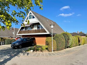Une maison à deux étages avec un toit en pente, un garage et une voiture noire garée dans l’allée.