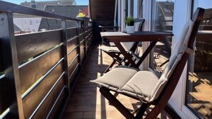 A balcony with a wooden chair, a small table with a potted plant, and a view of buildings in the background. - Maisonette apartment near the beach - beach chair included! (Dahme)