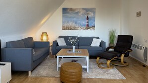 A modern living room with a grey sofa, a wooden coffee table, a rocking chair, and a painting of a lighthouse. - Maisonette apartment near the beach - beach chair included! (Dahme)