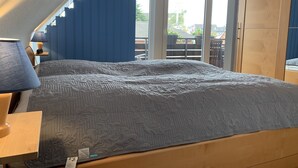 A bedroom with a bed, a nightstand, a lamp, and a view of the outdoors through a window. - Maisonette apartment near the beach - beach chair included! (Dahme)