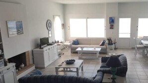 A spacious living area with a sofa, coffee table, and a dining table. There is a kitchen area with cabinets and a refrigerator. - Charming 4-bed Villa in Pefkali (Corinth)