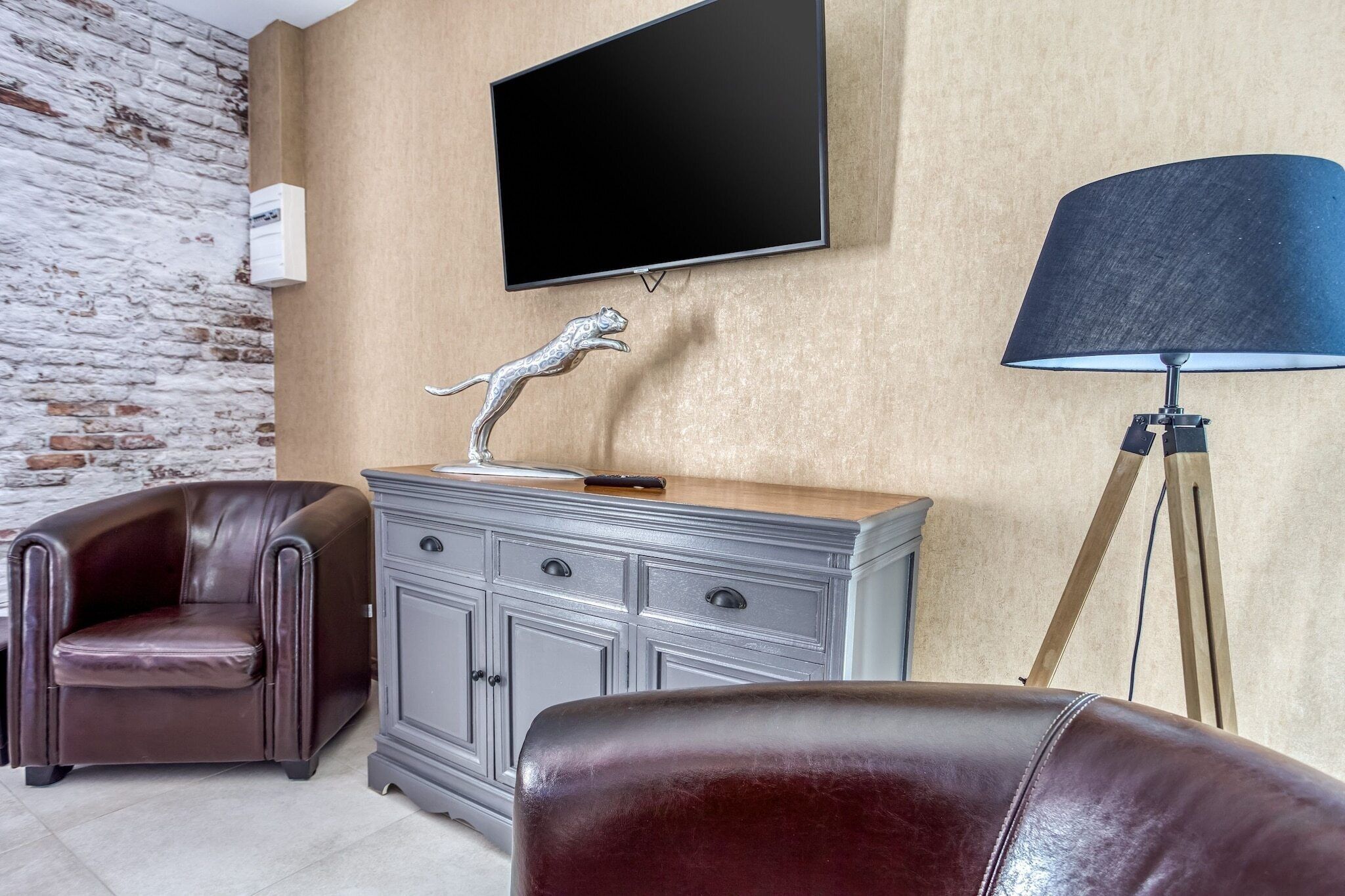 A modern living room with a leather armchair, a grey cabinet, a mounted TV, and a floor lamp.