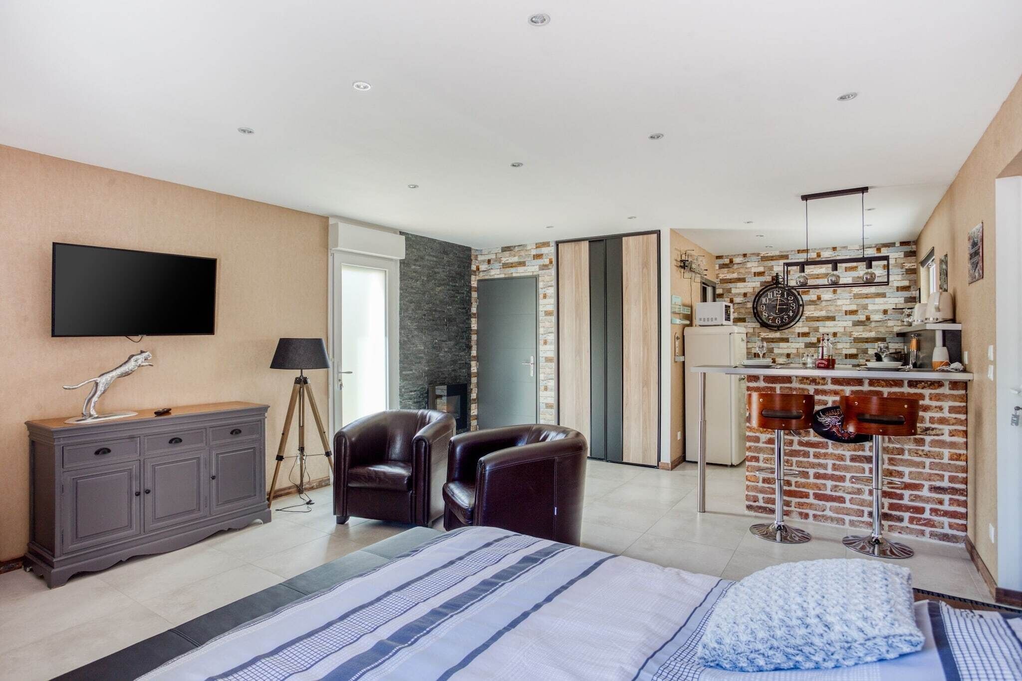 A modern hotel room with a large bed, a desk, a TV, and a kitchenette.