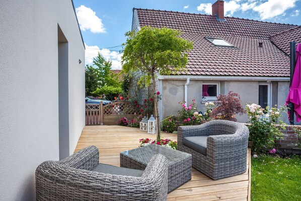 A patio with wicker furniture, a wooden deck, and a house with a tiled roof.