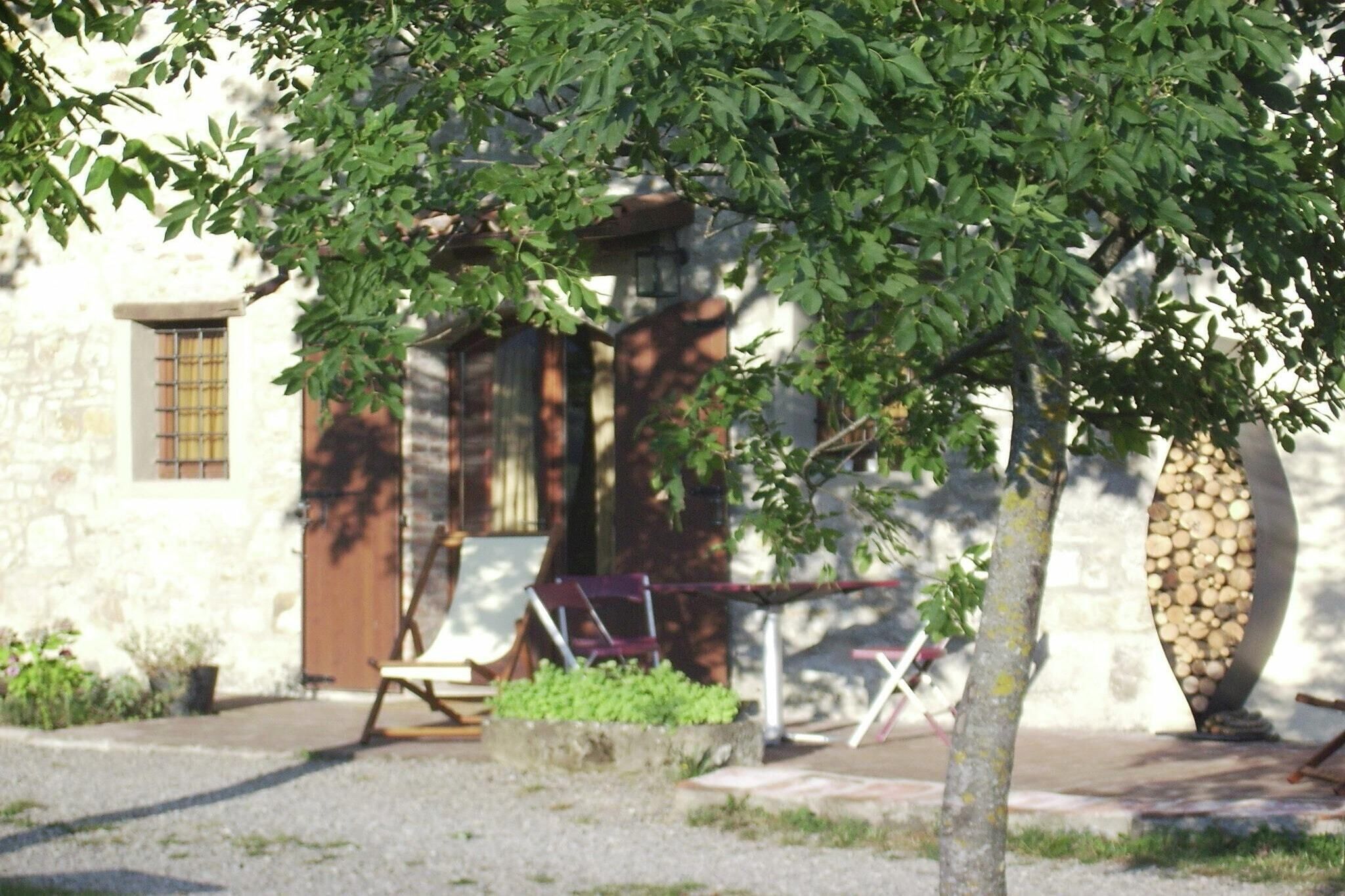 A stone building with a wooden door and windows, a bench, and a tree in the foreground.