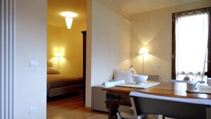 Una camera d'albergo con pavimento in legno, un tavolo da pranzo con sedie, un divano e due abat-jour.