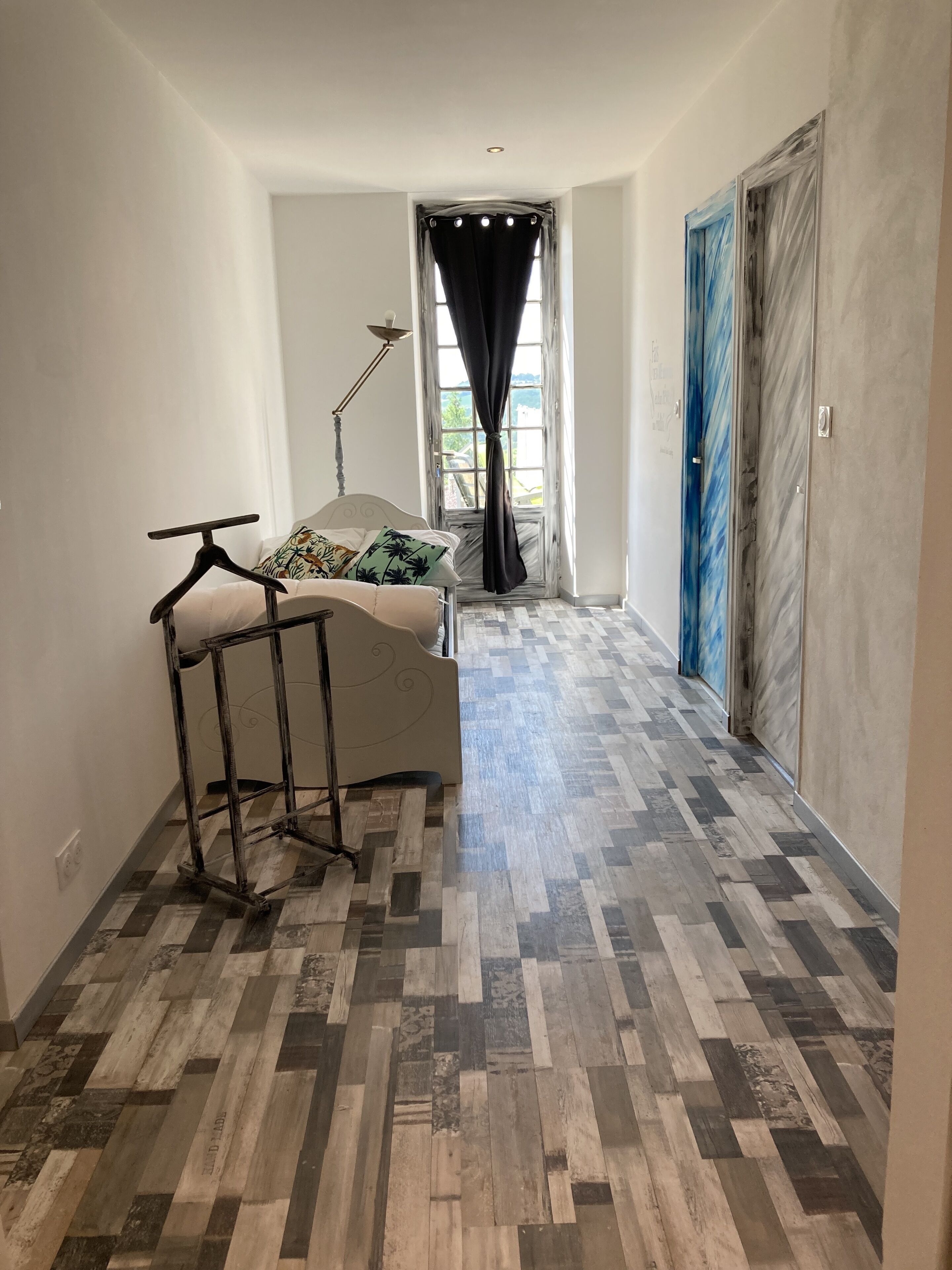 Una habitación con cama, perchero y ventana con cortinas.