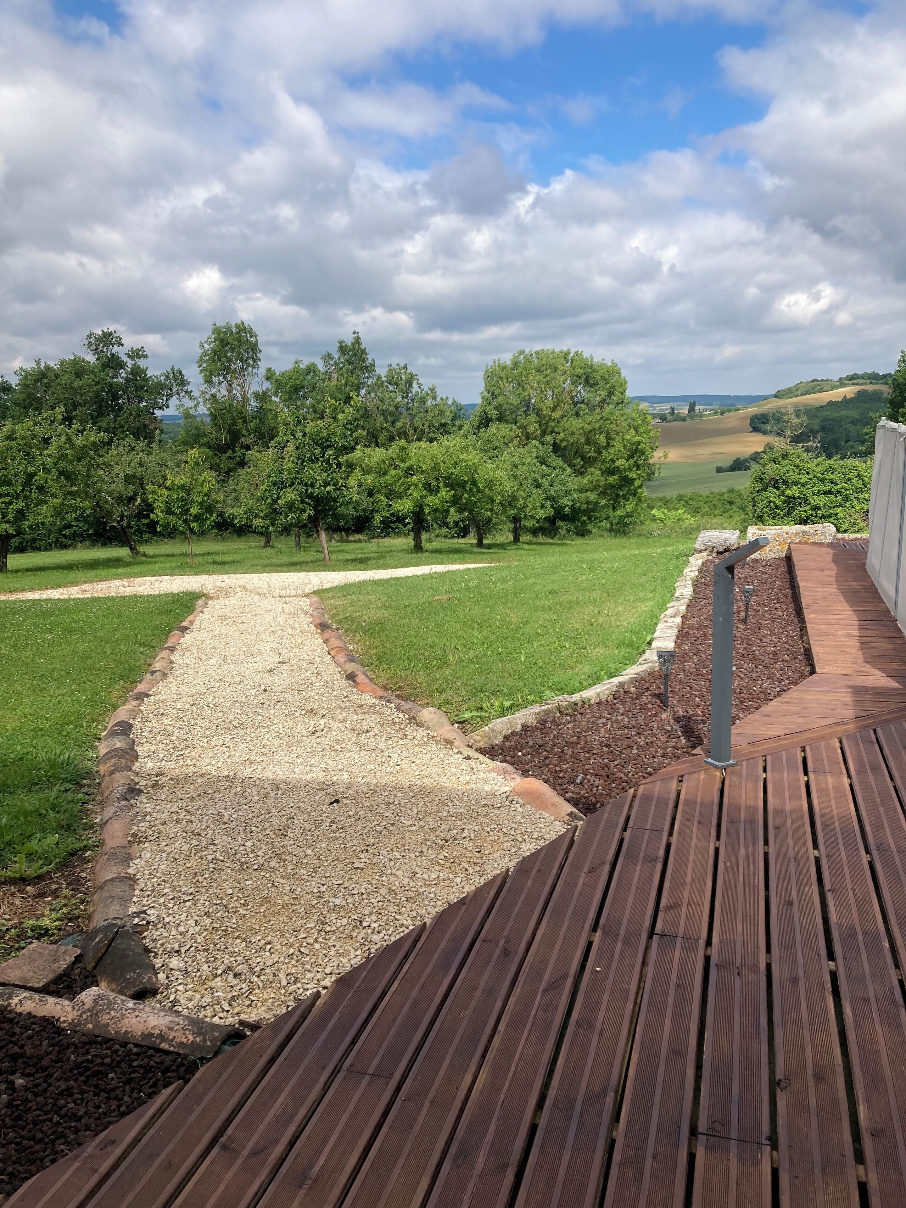 Un patio in legno con un sentiero di ghiaia che conduce a una zona erbosa alberata.