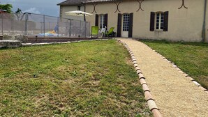 A building with a tiled roof, a paved pathway, and a fenced area with outdoor furniture. - Country house with swimming pool (Coulx)