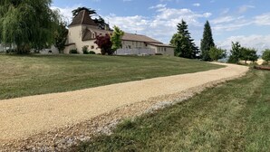 A gravel path leading to a house with a sloped roof and a large tree in the foreground. - Country house with swimming pool (Coulx)