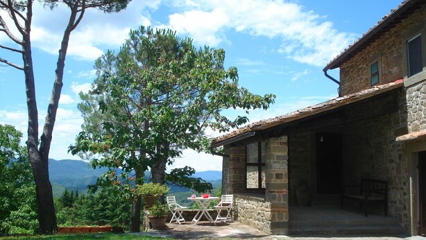 A stone building with a patio, outdoor seating, and a view of mountains.