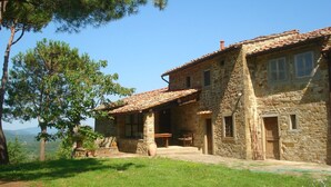A stone building with a tiled roof, a wooden bench, and a view of the surrounding landscape.