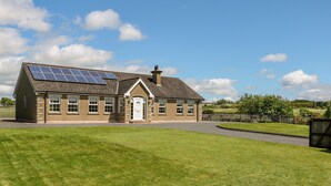 Ein zweistöckiges Haus mit geneigtem Dach, Solaranlage auf dem Dach, einer Haustür und einem eingezäunten Vorgarten.