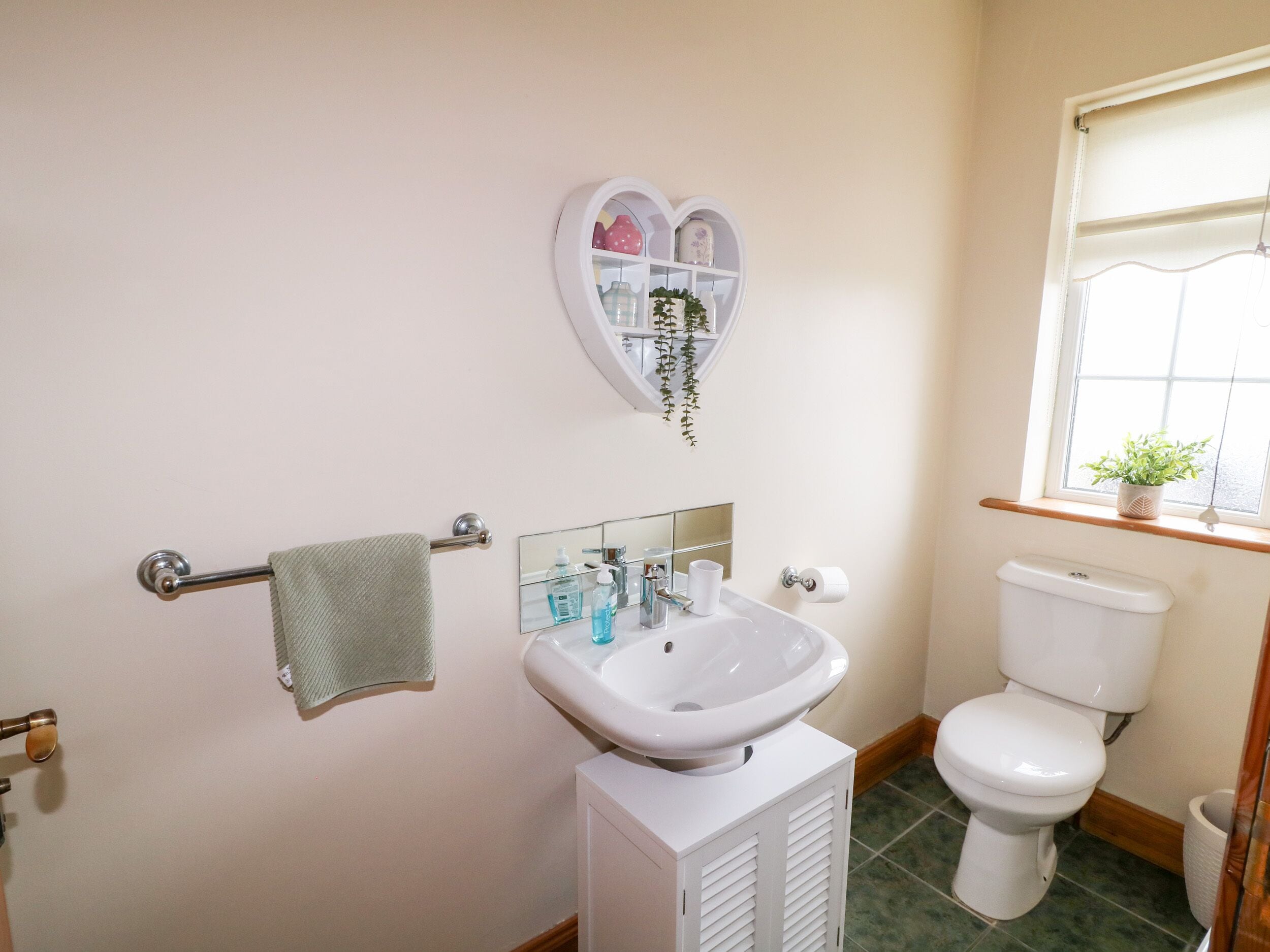 Een badkamer met een witte wastafel, toilet en een hartvormige plank boven de spiegel.