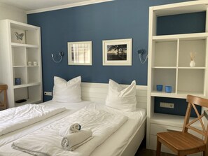 Une chambre avec deux lits, du linge de lit blanc, une chaise en bois et un mur bleu.