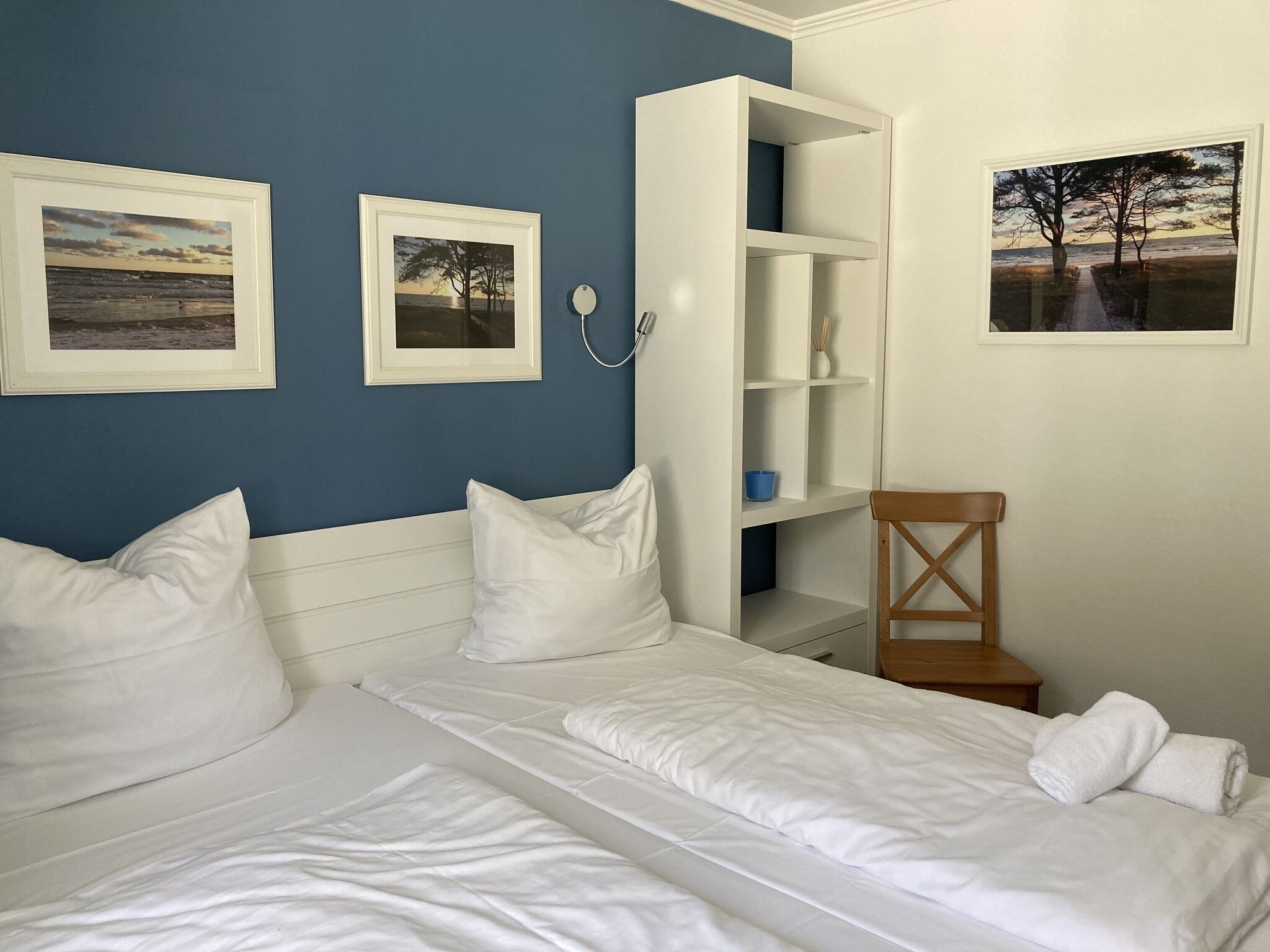 Une chambre avec deux lits, une armoire blanche et trois tableaux encadrés accrochés au mur.