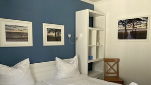 A bedroom with two beds, a white wardrobe, and three framed pictures on the wall. - Comfort plus apartment with 1 bedroom and balcony on the upper floor (Ostseebad Binz)
