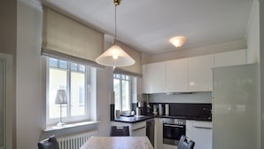 A modern kitchen with white cabinets, a wooden table, and black chairs. - Comfort plus apartment with 1 bedroom and balcony on the upper floor (Ostseebad Binz)