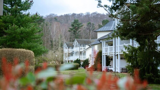 A large, multi-story building with a white exterior and a grey roof, surrounded by lush greenery and trees. - Comfort plus apartment with 1 bedroom and balcony on the upper floor (Ostseebad Binz)