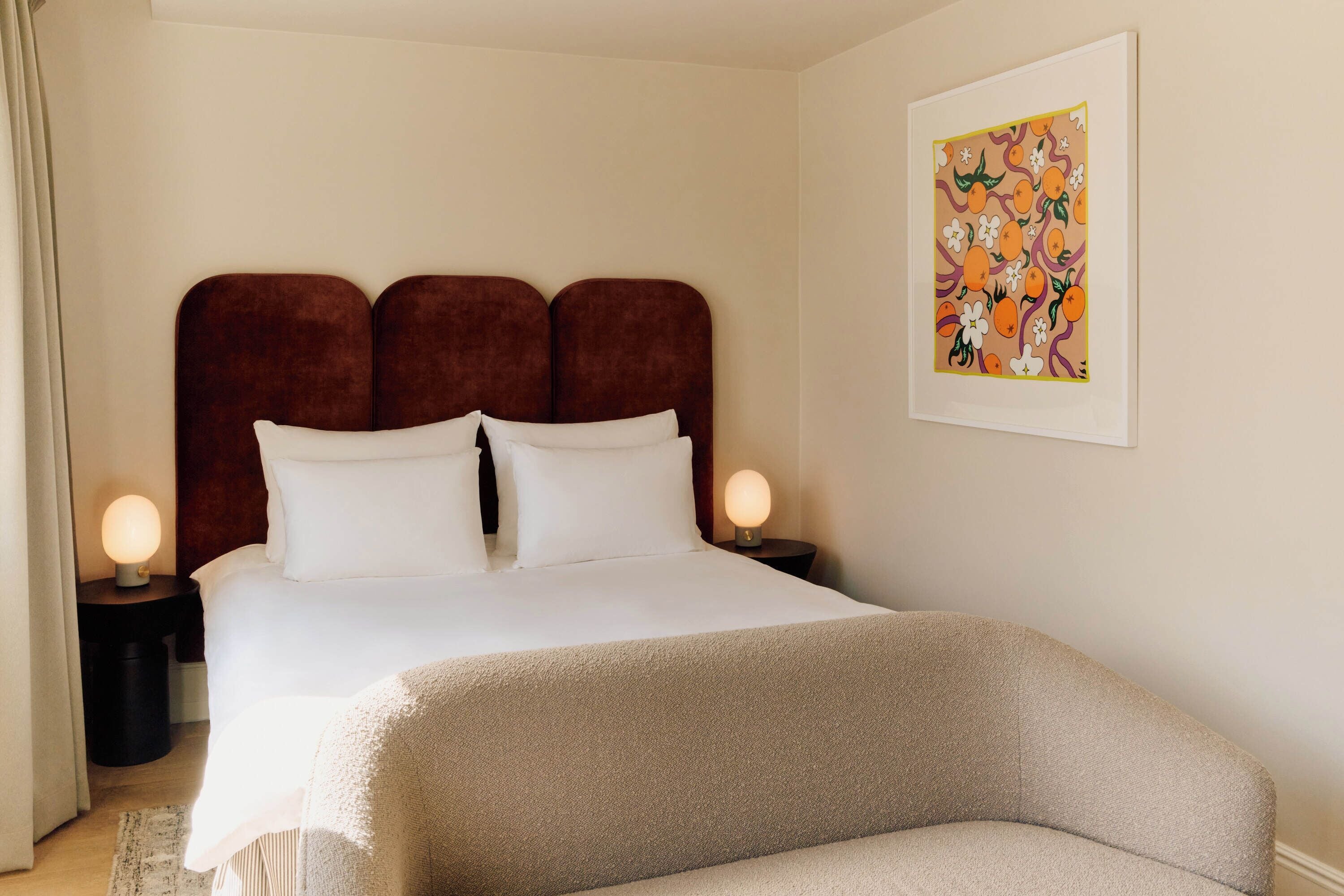 A neatly made bed with a brown headboard, two bedside lamps, and a framed artwork on the wall.
