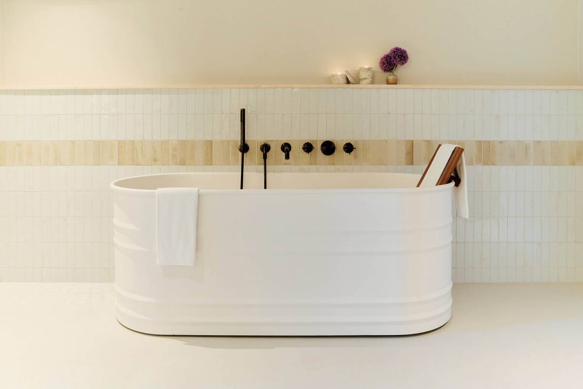 A white bathtub with a towel, a book, and a black showerhead against a tiled wall.