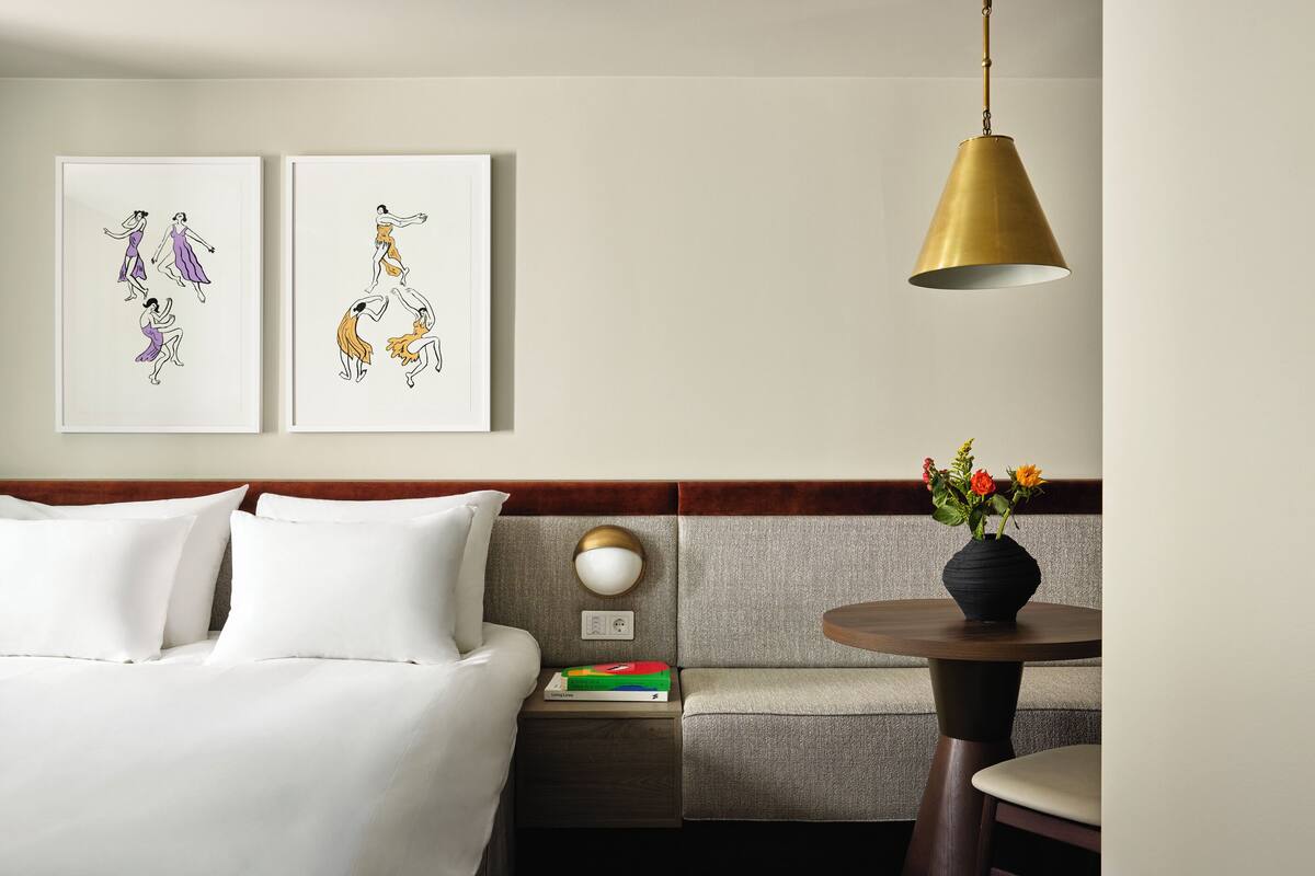 A hotel room with a bed, a sofa, a nightstand with a lamp, and a table with a vase of flowers.